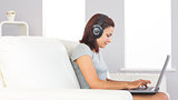 Cute casual woman witting on couch using her notebook and listening to music