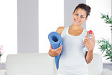 Young woman posing holding an exercise mat and a bottle in her living room