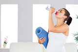 Attractive woman drinking out of a bottle while holding an exercise mat