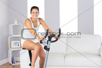 Joyful slim woman smiling at camera while training on an exercise bike