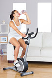 Cute fit woman drinking water while training on an exercise bike