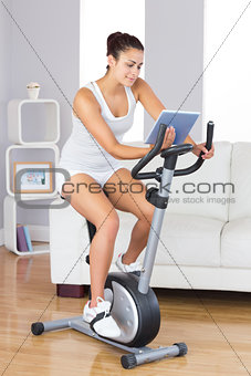 Content slim woman using her tablet while training on an exercise bike
