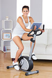 Happy training woman using an exercise bike while holding a tablet