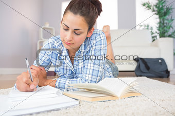 Gorgeous brunette student doing homework lying on the floor