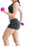 Mid section of slim young woman training her arms with pink dumbbells