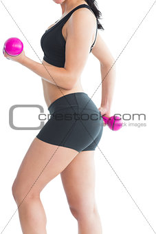 Mid section of slim young woman training her arms with pink dumbbells