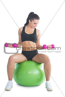 Sporty slim woman training her arms with dumbbells sitting on an exercise ball