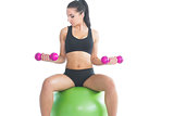 Concentrating sporty woman using dumbbells sitting on an exercise ball