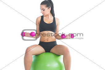 Concentrating sporty woman using dumbbells sitting on an exercise ball
