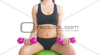 Mid section of slender fit woman training with dumbbells sitting on an exercise ball