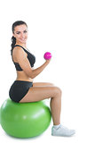 Cheerful active woman sitting on an exercise ball using pink dumbbells