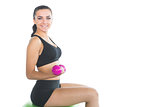 Beautiful slim woman using pink dumbbells sitting on an exercise ball