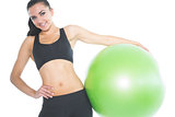 Cheerful brunette woman posing holding a green exercise ball