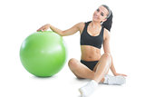 Cute slender woman posing sitting on the floor next to an exercise ball