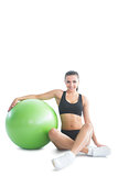 Front view of attractive brunette woman posing sitting next to an exercise ball