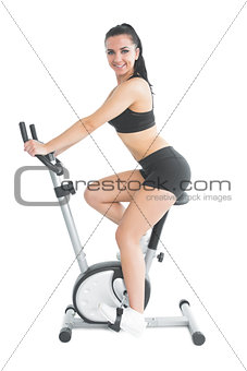 Slender fit woman training on an exercise bike smiling at camera