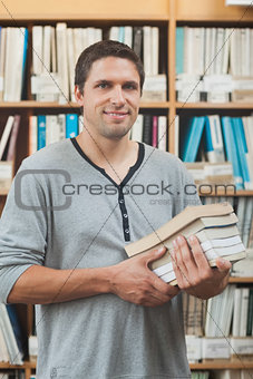 Mature student posing in library holding a pile of books