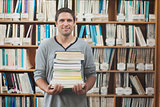 Attractive librarian holding a pile of books standing in library