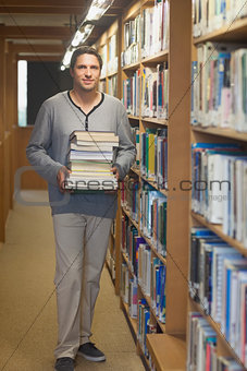 Attractive male librarian carrying a pile of books
