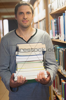 Handsome brunette librarian posing in library holding a pile of books