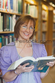 Cheerful mature female librarian posing holding an opened book
