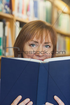 Content mature woman sitting in library holding a book