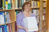 Cheerful mature librarian posing holding a stack of books