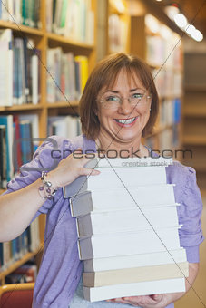 Happy female librarian holding a pile of books in a library