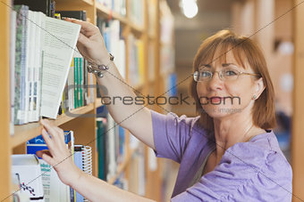 Mature female librarian taking a book off a shelf