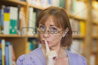 Mature female librarian giving a sign to be quiet standing in library