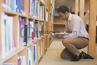 Attractive casual man reading a book in library
