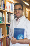 Attractive intellectual man posing in library holding a book
