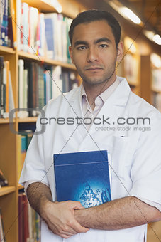 Serious intellectual man posing in library with a book