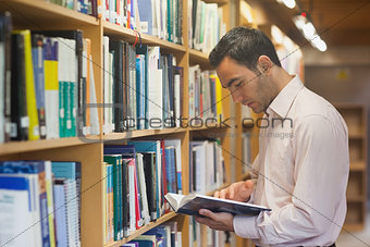Intellectual man reading a book standing in library