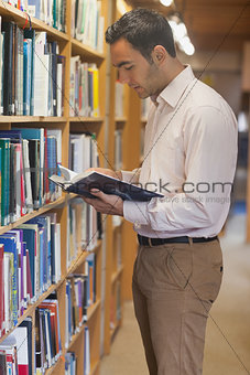 Handsome man reading concentrated a book standing in library