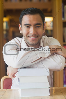 Attractive man posing in library leaning on a pile of books