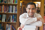 Cheerful attractive man posing leaning on a stack of books in library