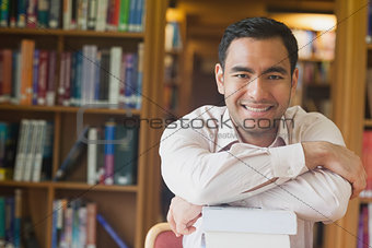 Cheerful attractive man posing leaning on a stack of books in library