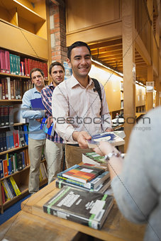 Attractive man handing a book to the female librarian