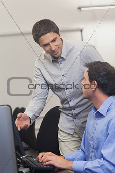 Attractive teacher talking to his student in computer class