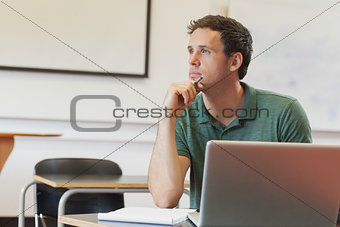 Thoughtful handsome mature student sitting in classroom while learning