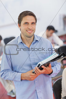 Cute male teacher holding some files while posing in his classroom