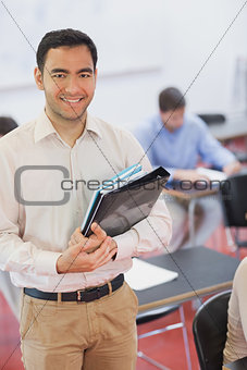 Handsome black haired teacher posing in his classroom holding some files