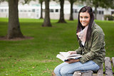 Cheerful brunette student sitting on bench reading