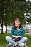 Smiling casual student sitting on bench reading