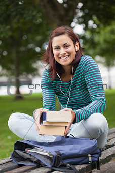 Cheerful casual student sitting on bench holding books