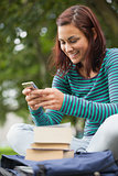 Cheerful casual student sitting on bench texting