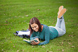 Happy casual student lying on grass reading