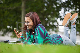 Smiling casual student lying on grass texting