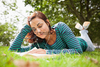Smiling casual student lying on grass reading a book